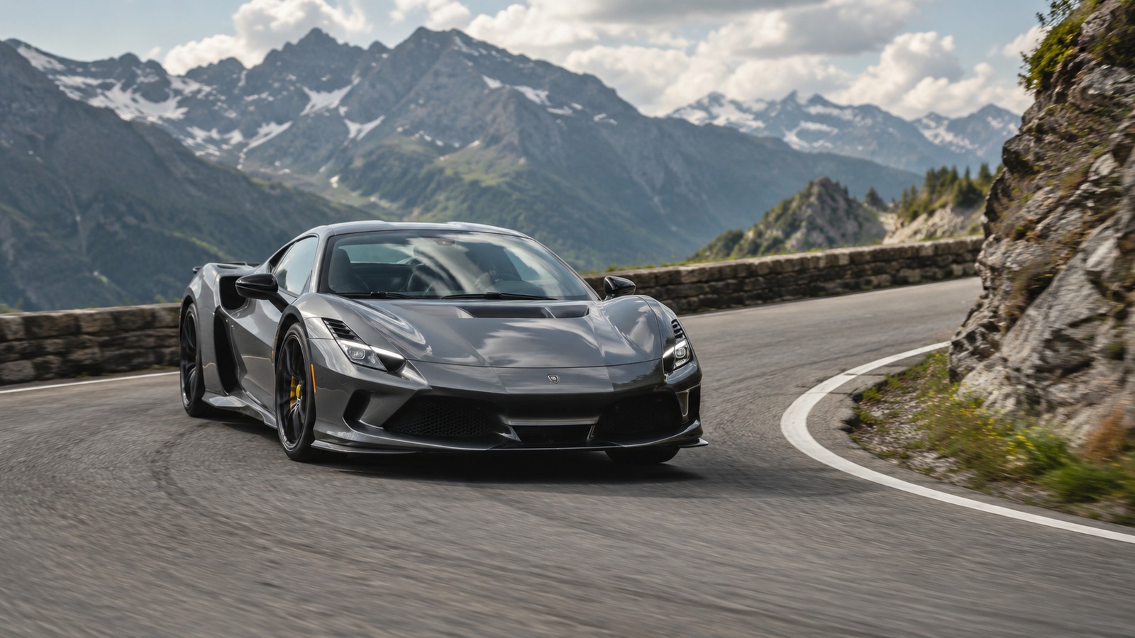 Ein moderner graphitfarbener Supersportwagen fährt durch eine enge Kurve auf einer alpinen Bergstrasse.