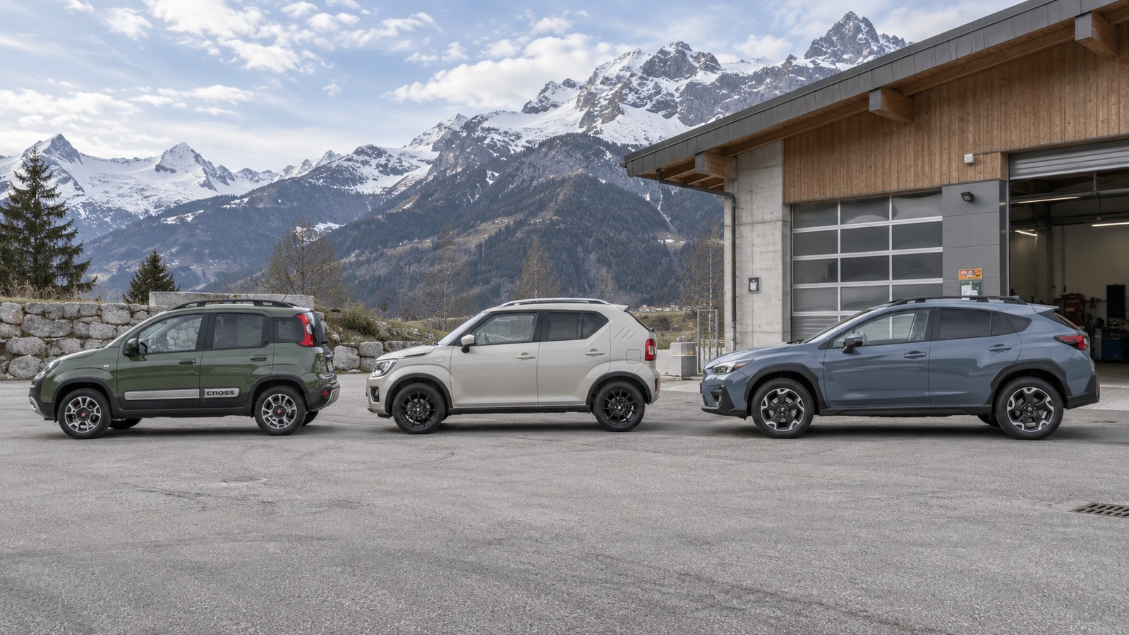 Fiat Panda Cross, Suzuki Ignis und Subaru Crosstrek stehen seitlich nebeneinander vor einer Werkhalle in den Alpen.