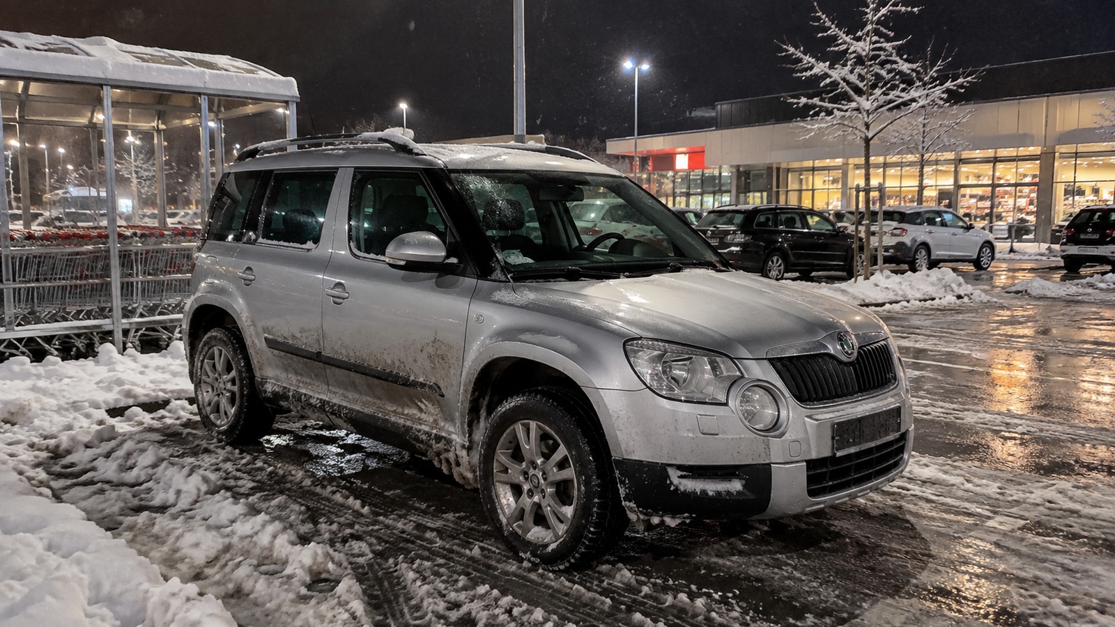 Ein gebrauchter Skoda Yeti steht bei Schneefall auf einem nassen Supermarktparkplatz.